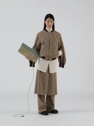 Model standing against a plain white background holding a vintage computer keyboard in the GU x Rokh collaboration collection.