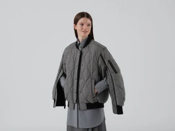 Model wearing a grey houndstooth quilted puffer jacket and grey shirt against a plain white background.