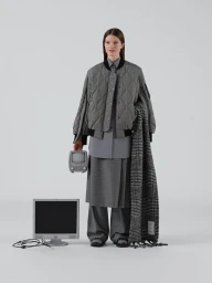 Model wearing a grey quilted bomber jacket holding a small retro monitor against a plain white background