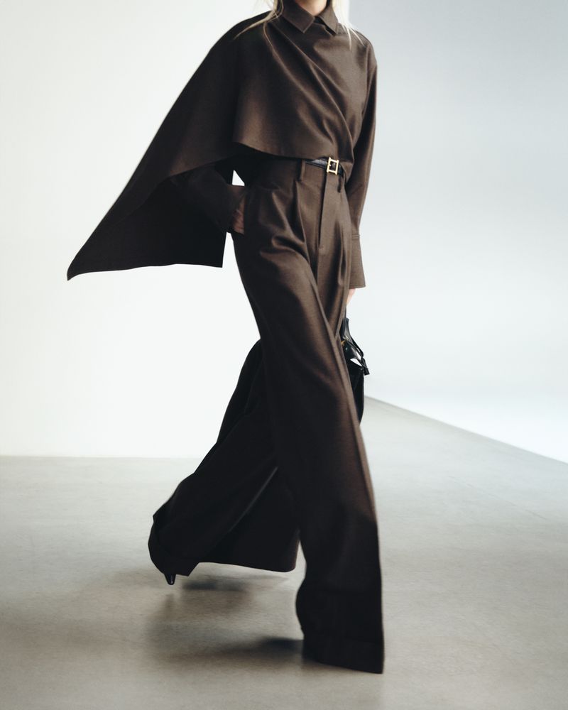 Model wearing a brown cape top and matching high-waisted trousers against a neutral studio background.