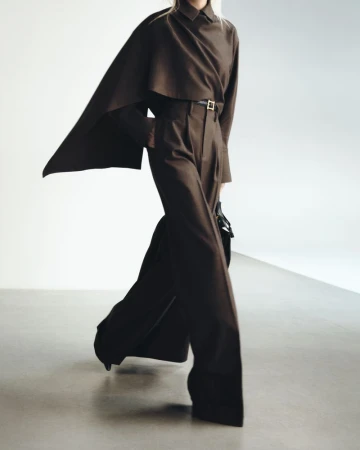 Model wearing a brown cape top and matching high-waisted trousers against a neutral studio background.