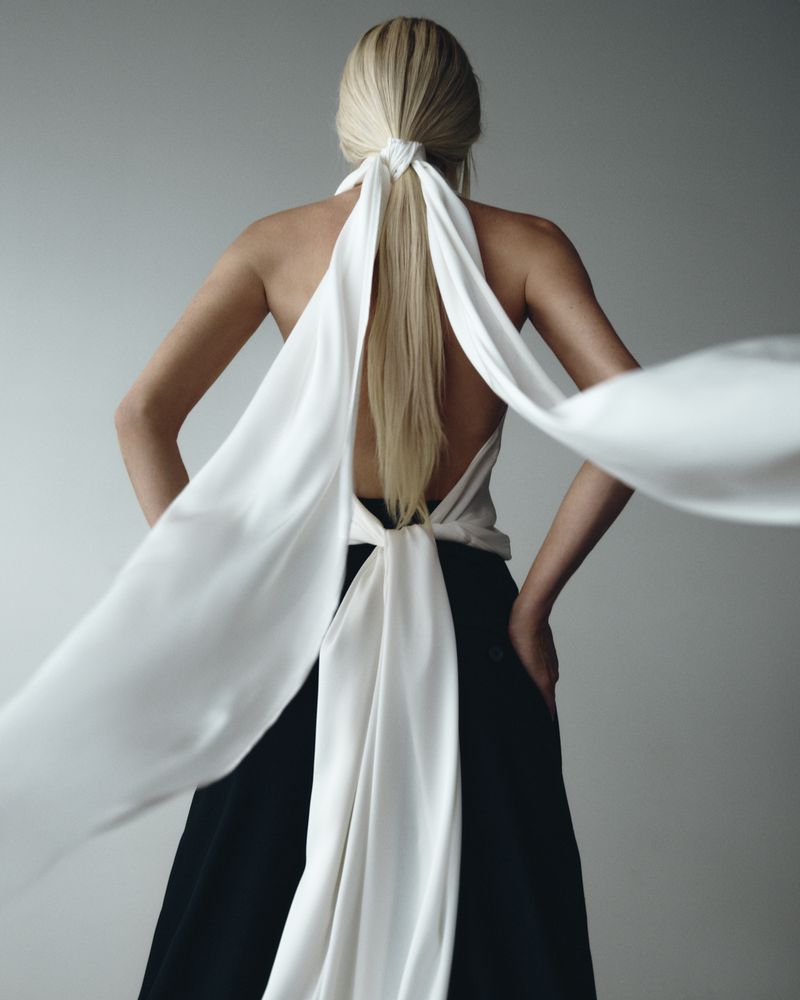 Back view of a fair-skinned adult female with blonde hair, wearing a halter top and black pants in a studio setting.