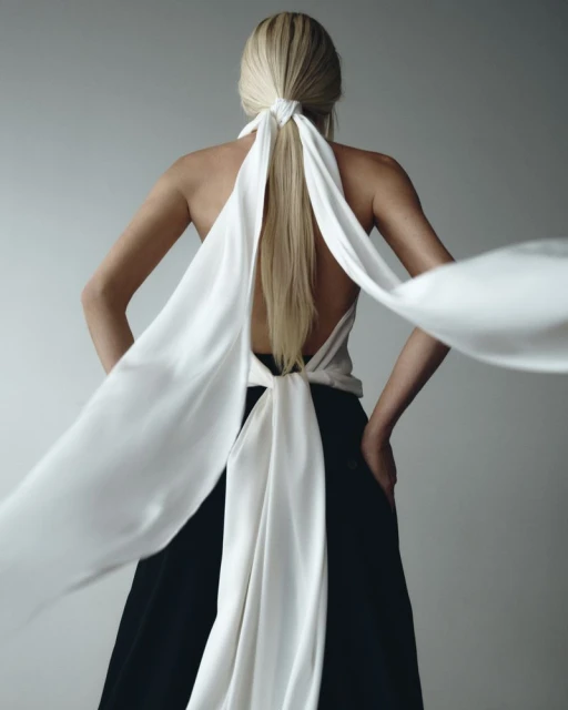 Back view of a fair-skinned adult female with blonde hair, wearing a halter top and black pants in a studio setting.