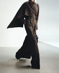 Model wearing a brown cape top and matching high-waisted trousers against a neutral studio background.