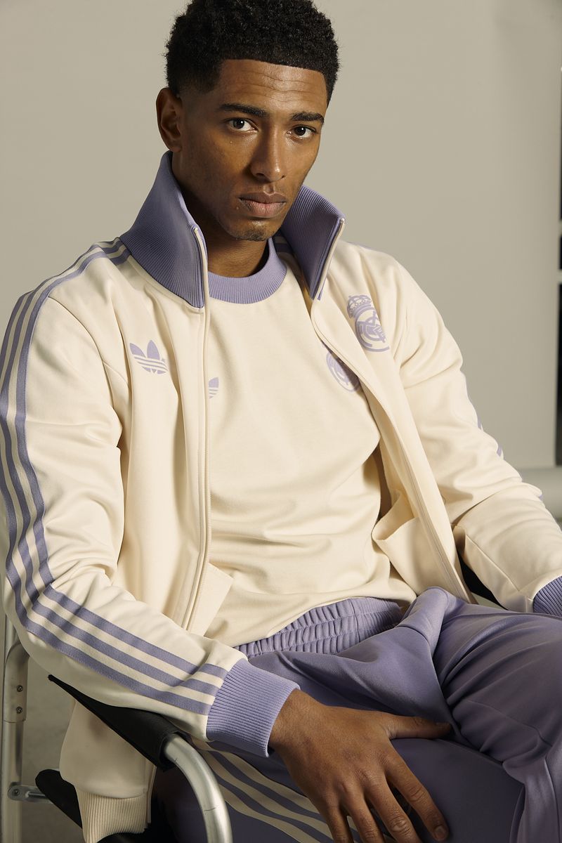 Portrait of handsome adult male athlete wearing vintage Adidas tracksuit with Real Madrid logo, sitting in wheelchair against studio backdrop.