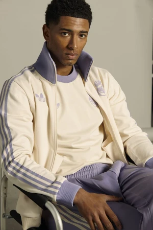 Portrait of handsome adult male athlete wearing vintage Adidas tracksuit with Real Madrid logo, sitting in wheelchair against studio backdrop.