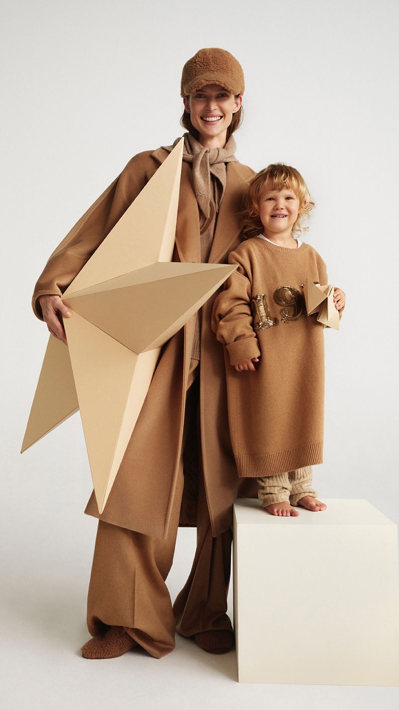 A woman and child in matching tan outfits pose in front of a white background, holding geometric cardboard shapes. They are both smiling.