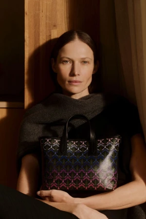 Elegant woman holding a patterned leather handbag in a softly lit, natural-toned indoor setting, fashion and accessories shoot.