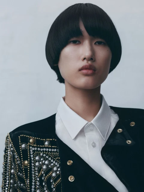 Close-up portrait of a young Asian woman with short, straight black hair, wearing an embellished black blazer and white collared shirt.