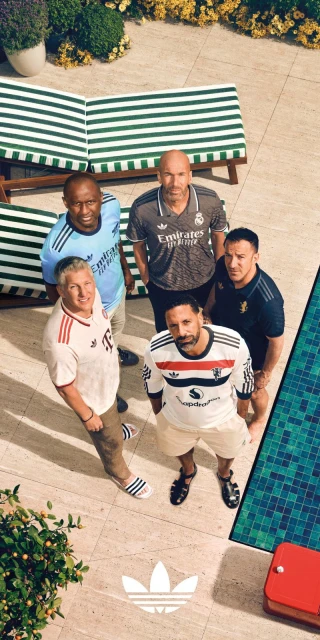 Group of five adult male soccer players wearing team jerseys in an outdoor setting, photographed from a high angle with pool and plants.