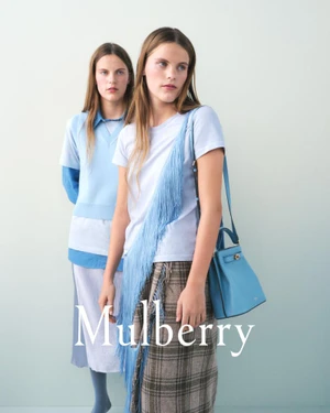 Two female models posing for the Mulberry T2 campaign against a pale gradient backdrop wearing blue apparel and holding a blue handbag
