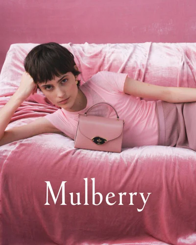 Model with dark hair reclining on a pink velvet sofa next to a pink leather handbag for Mulberry