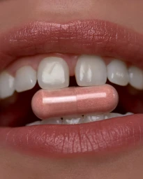 Close-up macro shot of lips slightly parted with a pink supplement capsule held between white teeth.