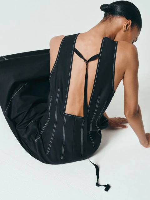 Back view of a black dress with white stitching detail, worn by an adult female in a studio setting against a white background.