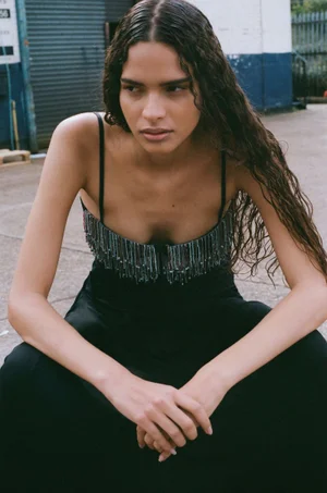 Model with long damp hair wearing a black spaghetti strap top with beaded fringe in an outdoor setting