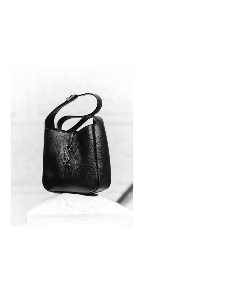 Black leather YSL handbag on a white concrete pillar, presented in a minimalist black and white fashion advertisement, clean modern aesthetic.
