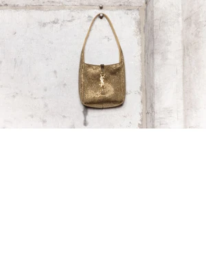 Gold crystal-embossed shoulder bag with metallic YSL hardware hanging on a distressed concrete wall surface.