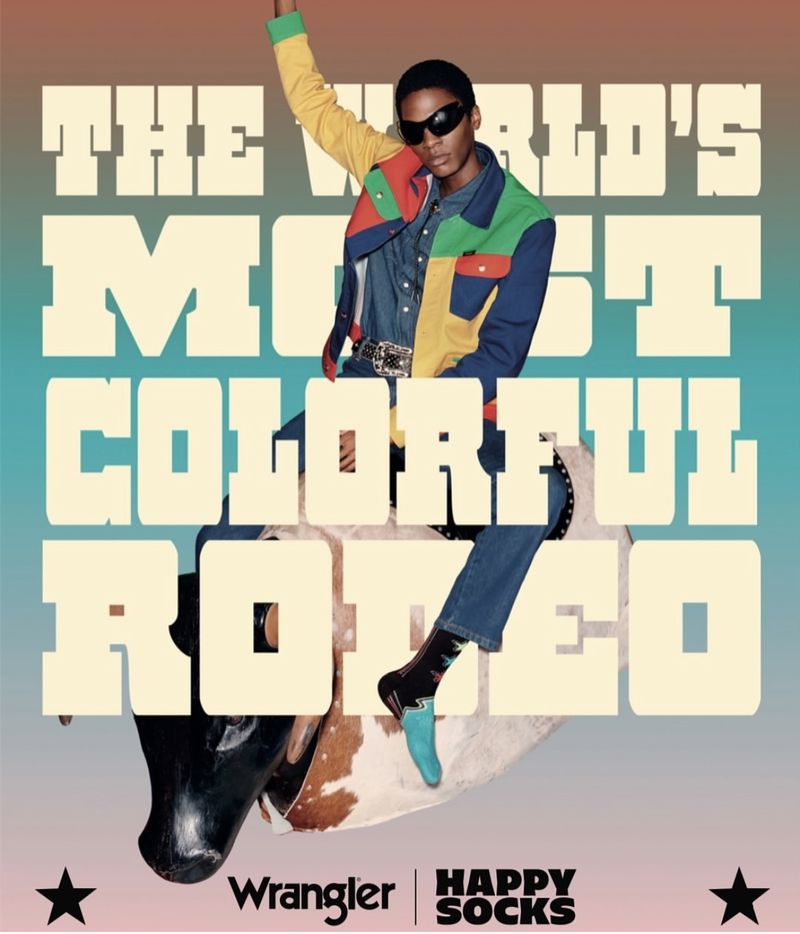 Fashion model wears colorful jacket and jeans, posing on a bull sculpture against a gradient background, promoting Wrangler and Happy Socks.