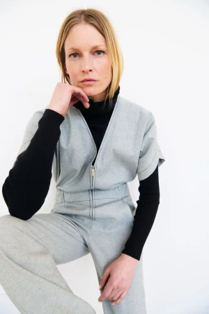 Model Hartje Andresen wearing a grey zipped jumpsuit over a black turtleneck against a white background