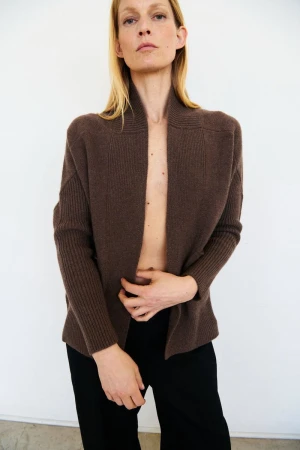 Model wearing a brown open-front knit cardigan and black pants against a plain white background.