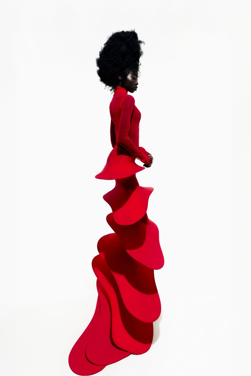 Elegant woman in a vibrant red gown with sculptural ruffles, set against a stark white background, showcasing haute couture fashion.