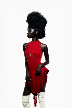 Black woman with voluminous afro wearing a red fringed dress and white knee-high boots against a plain white background