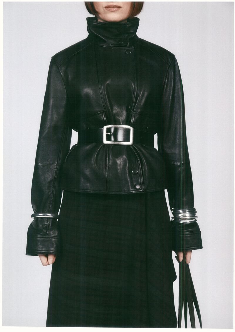 Model wearing a black leather jacket with a wide belt and silver bracelets against a seamless background
