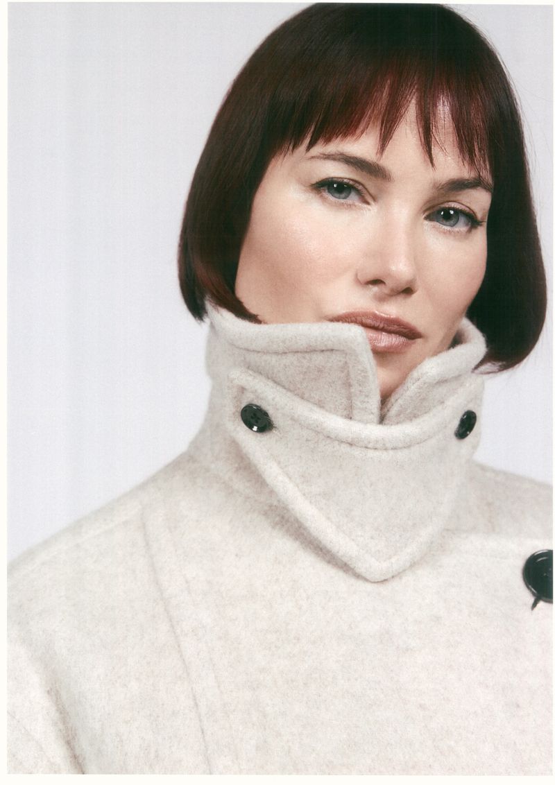 Portrait of a woman wearing a cream wool coat with a high collar and dark button details against a white background