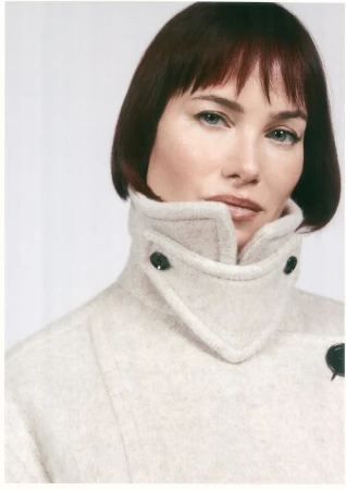 Portrait of a woman wearing a cream wool coat with a high collar and dark button details against a white background
