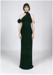 Woman in a long black one-shoulder evening gown with a floral arm accent standing against a seamless white background