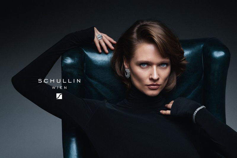 Model wearing a black turtleneck and diamond jewellery posing on a dark leather armchair for a Schullin Wien campaign