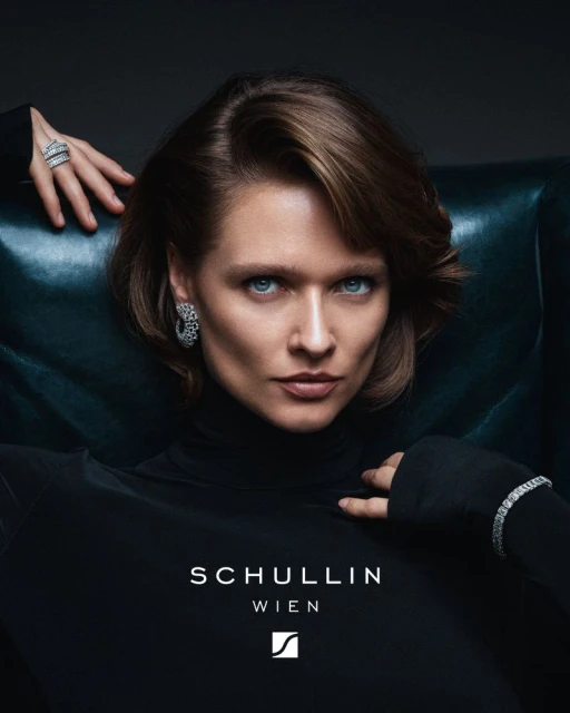 Elegant woman in a black turtleneck sweater and adorned with diamond jewelry posing in front of dark-green leather chair.