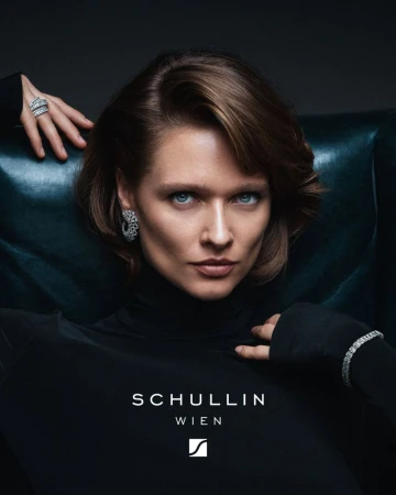 Elegant woman in a black turtleneck sweater and adorned with diamond jewelry posing in front of dark-green leather chair.
