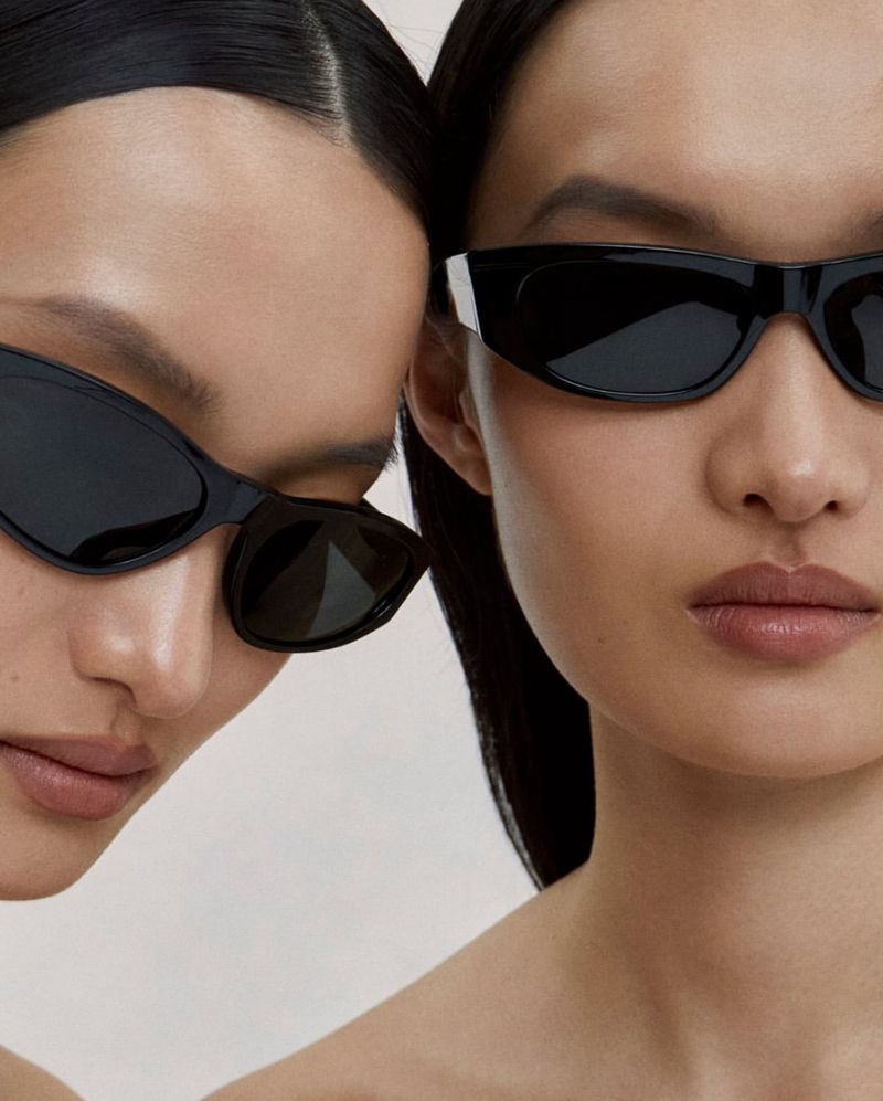 Close-up portrait of two models wearing black sunglasses for the Oliver Peoples Fai II and Fai III campaign.