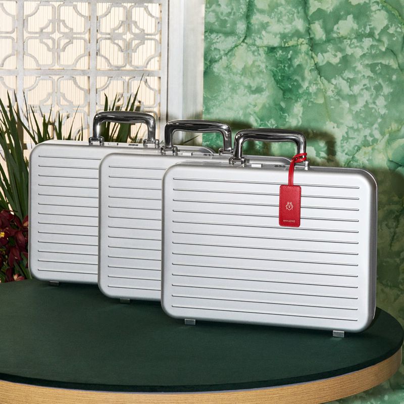 Three identical silver briefcases are arranged on a green table against an ornate white and green patterned background in an indoor setting.