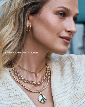 Close-up of a blonde woman wearing layered gold and diamond necklaces and gold hoop earrings for Stephanie Gottlieb jewelry.