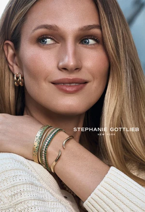 Close-up portrait of a woman wearing gold hoop earrings and layered gemstone bangles on her wrist for Stephanie Gottlieb.