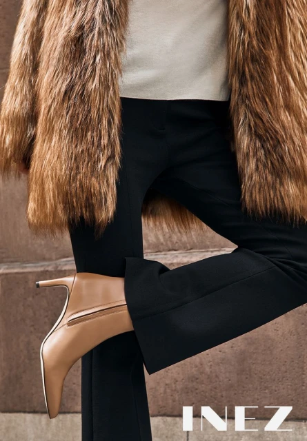 Fashion shot featuring a light brown heeled boot, black trousers, and a furry brown coat, captured in a close-up studio setting.