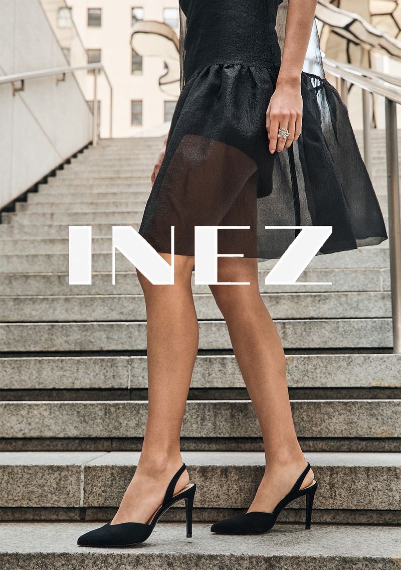 Close-up on a woman's legs and feet on concrete steps wearing black slingback heels and a black short skirt. 