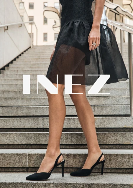 Close-up on a woman's legs and feet on concrete steps wearing black slingback heels and a black short skirt. 