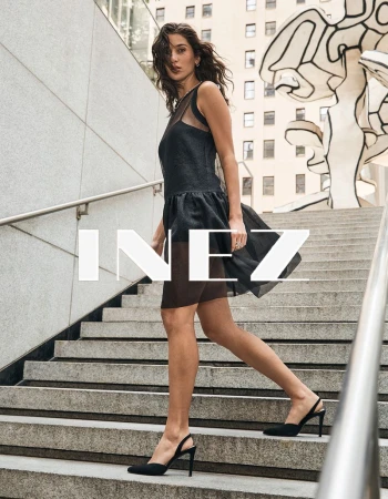 Model in a black sheer dress walking down outdoor stone stairs with metal handrails