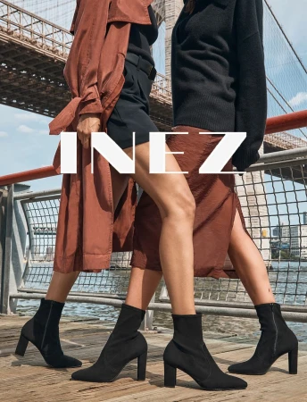 Two women wearing black sock boots stand in front of the Brooklyn Bridge in an outdoor fashion shot on a wooden pier.