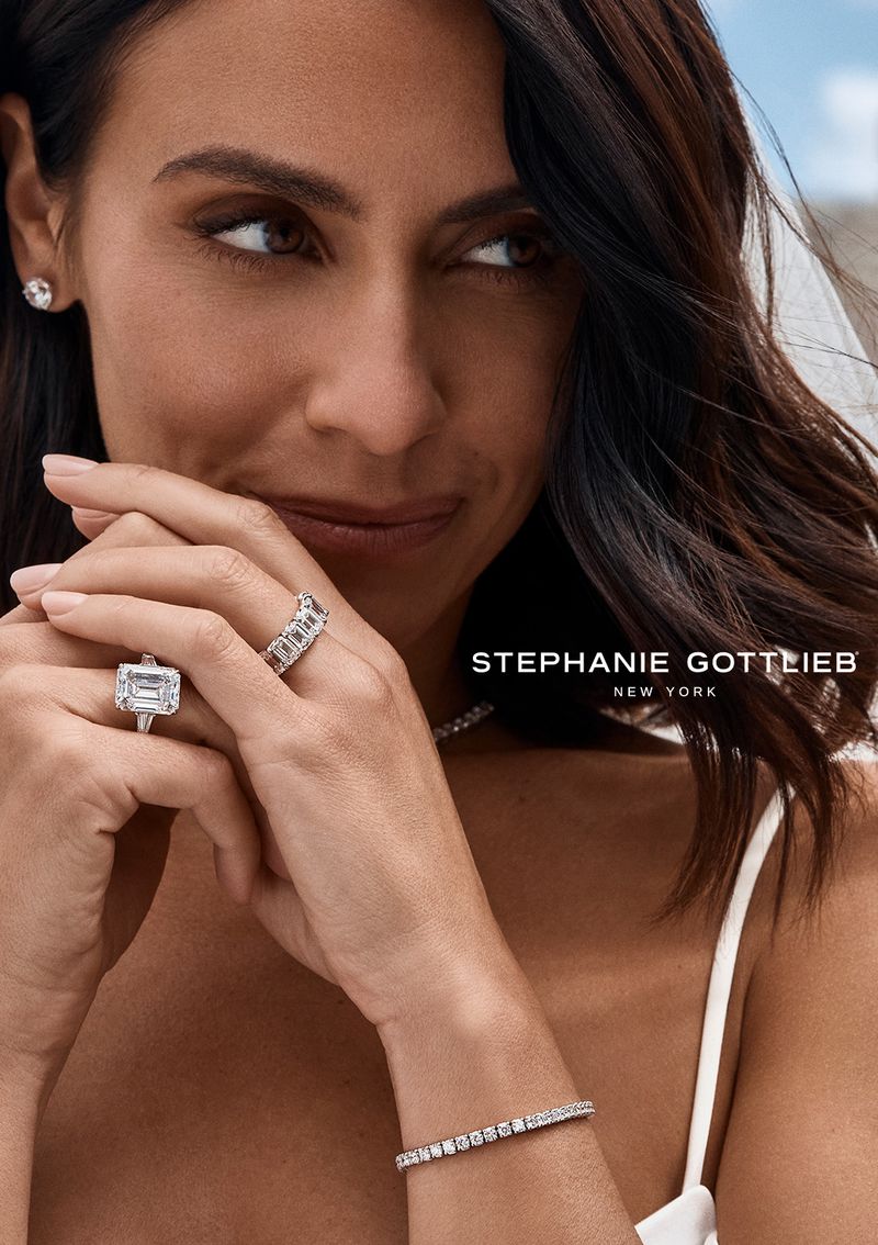 Elegant woman showcasing Stephanie Gottlieb New York jewelry: a prominent emerald-cut ring, tennis bracelet, and other diamond rings.