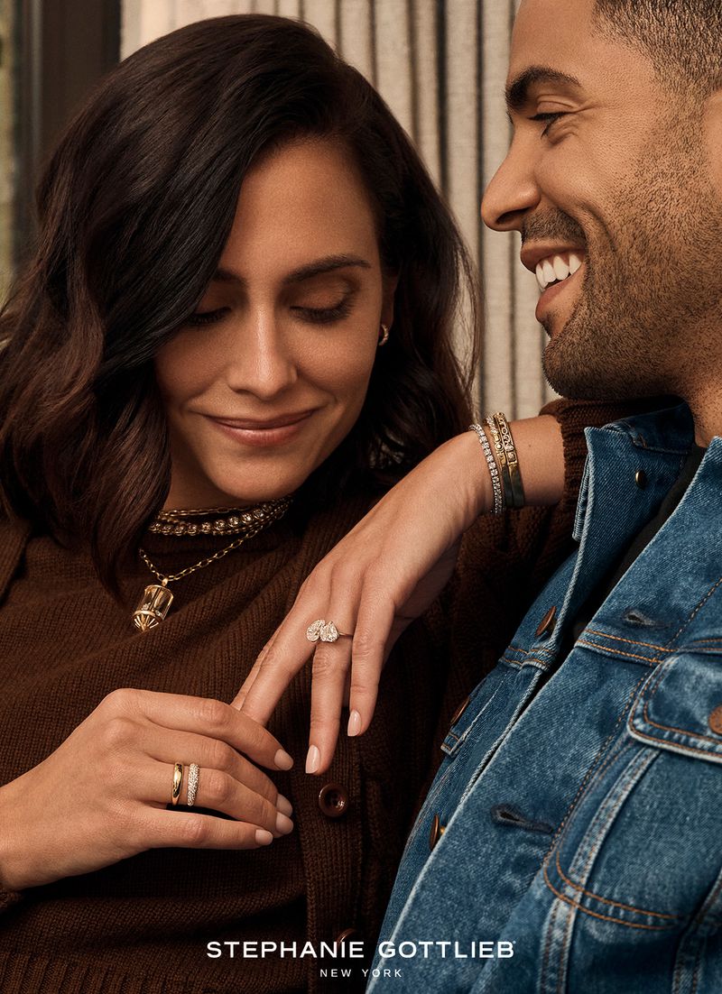 Close up of a smiling couple in casual clothing. The woman is wearing gold rings and necklaces. The man is in a blue jean jacket.
