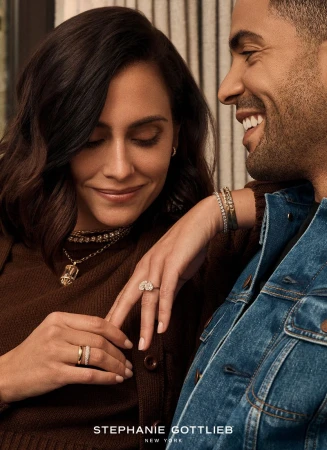 Close up of a smiling couple in casual clothing. The woman is wearing gold rings and necklaces. The man is in a blue jean jacket.