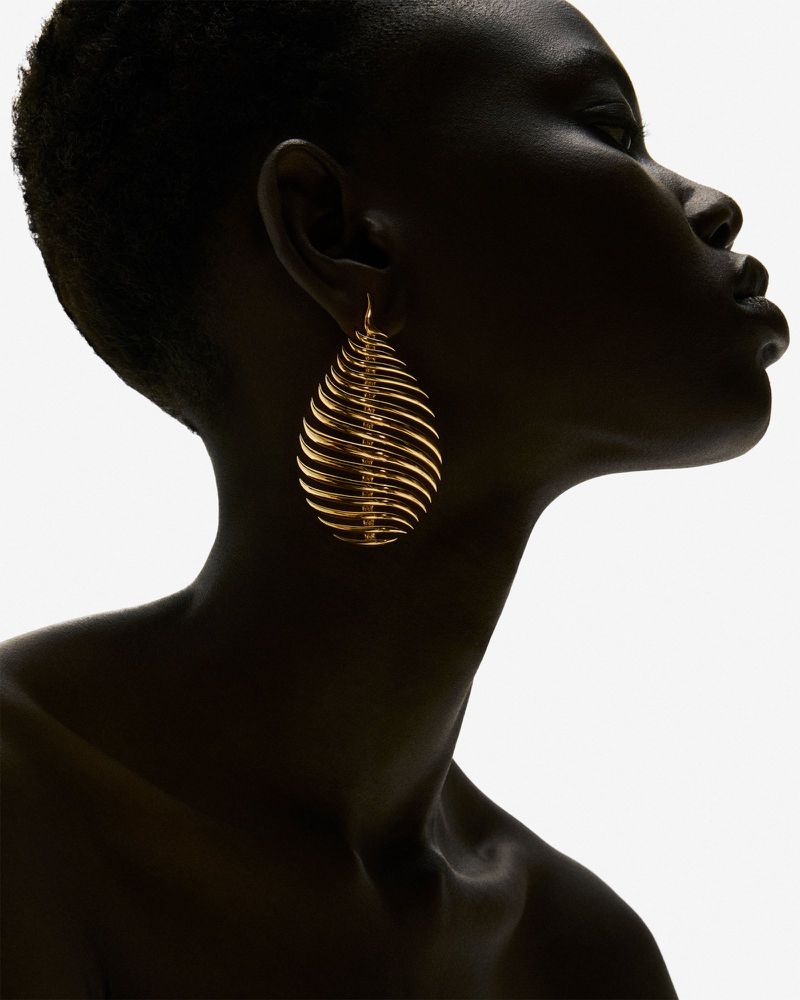Close-up shot of a Black woman in profile wearing a gold earring; the white background creates a stark contrast.
