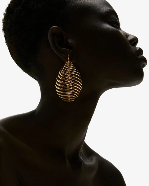 Close-up shot of a Black woman in profile wearing a gold earring; the white background creates a stark contrast.