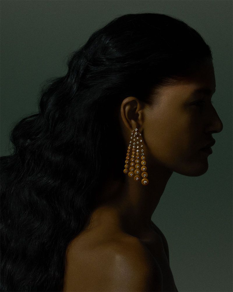 Profile portrait of a model wearing ornate dangling drop earrings against a dark green studio background