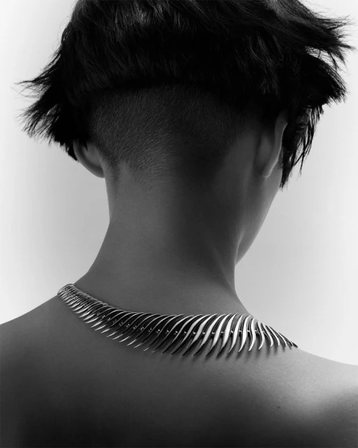 Back view of adult female with undercut and metallic necklace against white background. Fashion shot.