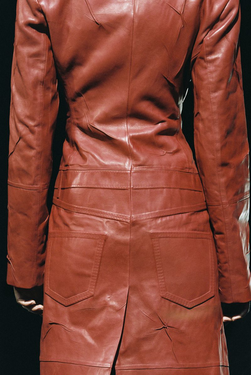 Rear view of a person wearing a red leather patchwork coat against a dark background, showcasing fashion and design details.
